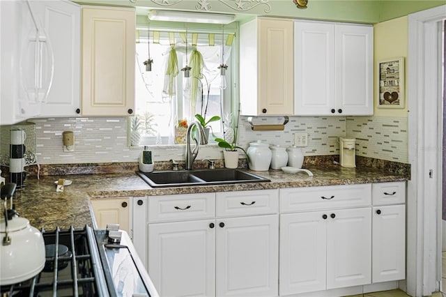 kitchen featuring backsplash, dark stone countertops, white cabinetry, and sink