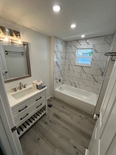 bathroom with hardwood / wood-style flooring, tiled shower / bath combo, and vanity