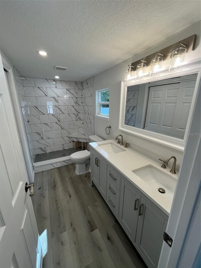 bathroom with vanity, a textured ceiling, tiled shower, hardwood / wood-style floors, and toilet