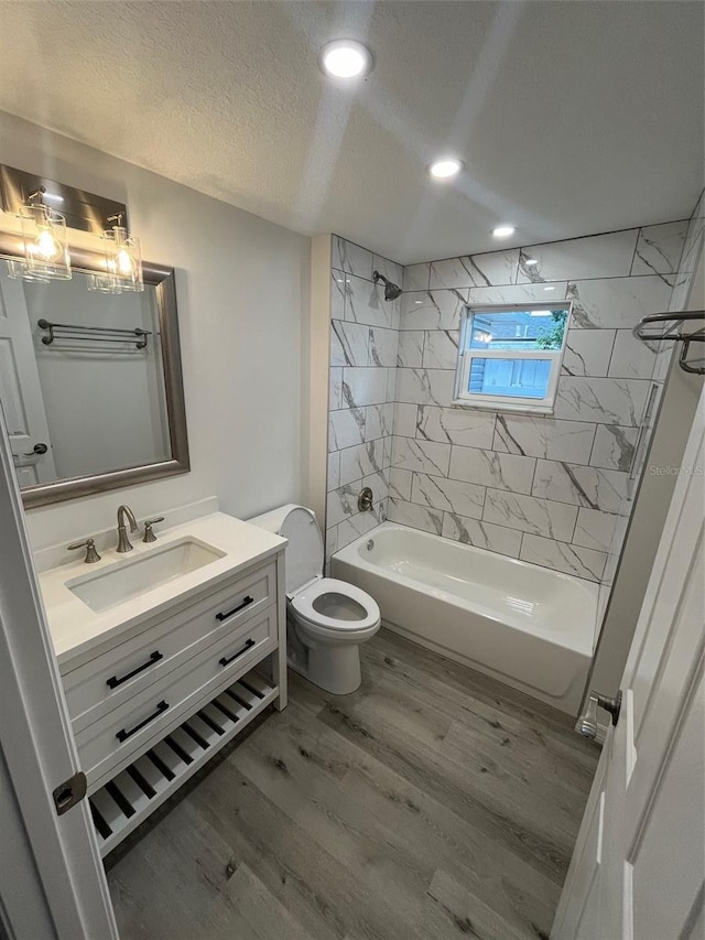 full bathroom with tiled shower / bath combo, hardwood / wood-style floors, a textured ceiling, toilet, and vanity