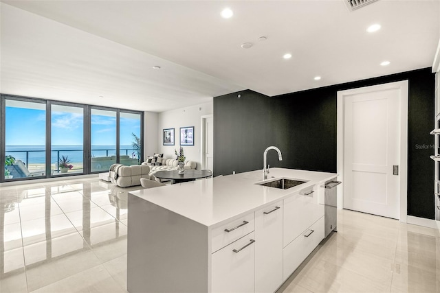 kitchen featuring light tile patterned flooring, sink, a center island with sink, white cabinetry, and a water view