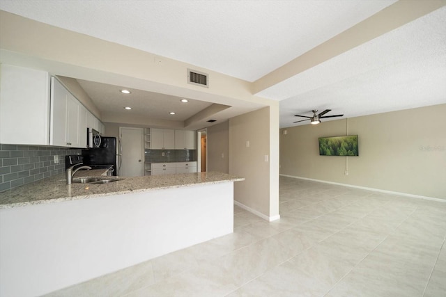 kitchen with kitchen peninsula, tasteful backsplash, light stone counters, ceiling fan, and white cabinetry