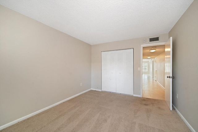 unfurnished bedroom featuring light colored carpet, a textured ceiling, and a closet