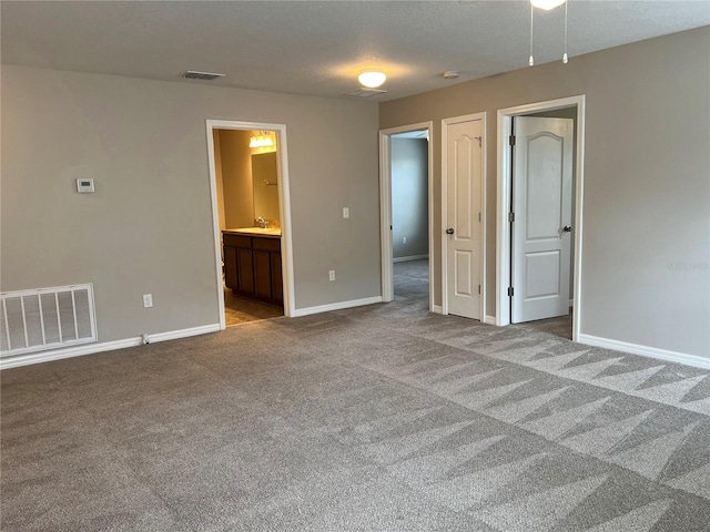 unfurnished bedroom with light carpet, ensuite bath, and a textured ceiling