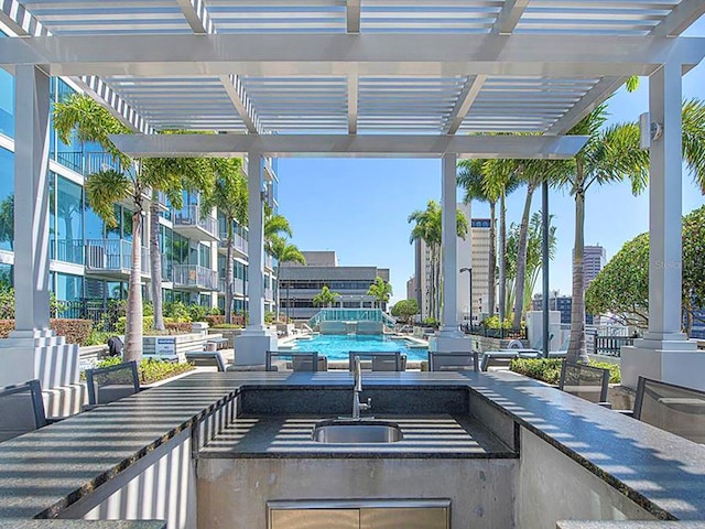 view of patio / terrace featuring a pergola, sink, a swimming pool with hot tub, and exterior kitchen