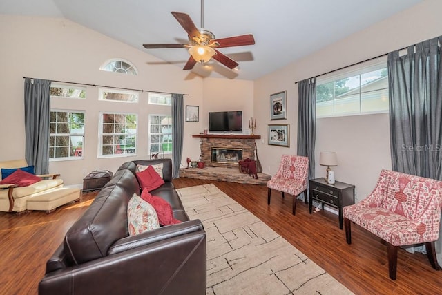 living room with a wealth of natural light, lofted ceiling, a stone fireplace, and hardwood / wood-style flooring