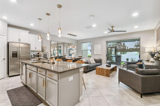 kitchen with white cabinets, an island with sink, sink, stone counters, and stainless steel appliances