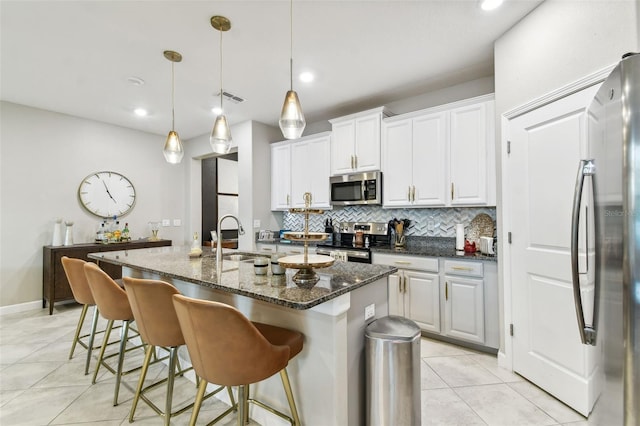 kitchen featuring appliances with stainless steel finishes, dark stone countertops, white cabinets, a kitchen island with sink, and sink