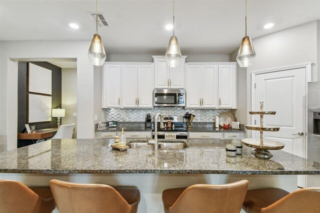 kitchen featuring sink, decorative light fixtures, white cabinetry, stainless steel appliances, and dark stone counters