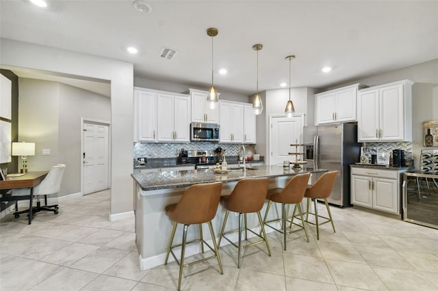 kitchen featuring dark stone counters, white cabinets, appliances with stainless steel finishes, and a kitchen island with sink