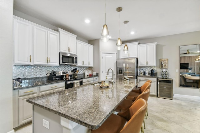 kitchen with stainless steel appliances, white cabinetry, a center island with sink, and wine cooler