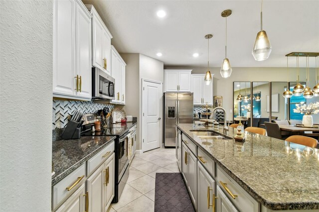 kitchen with a kitchen island with sink, sink, white cabinetry, appliances with stainless steel finishes, and decorative light fixtures