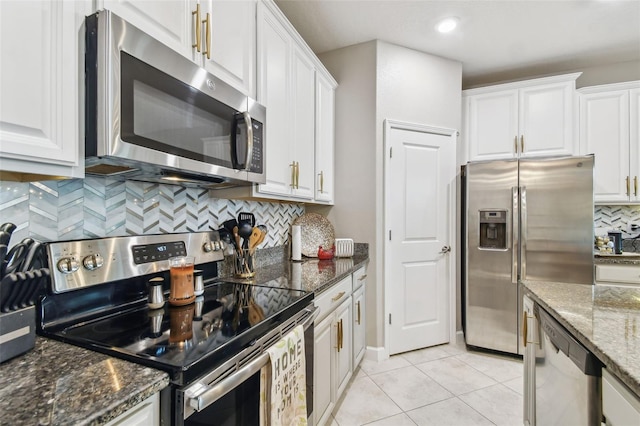 kitchen featuring light tile patterned floors, white cabinetry, stainless steel appliances, dark stone counters, and decorative backsplash