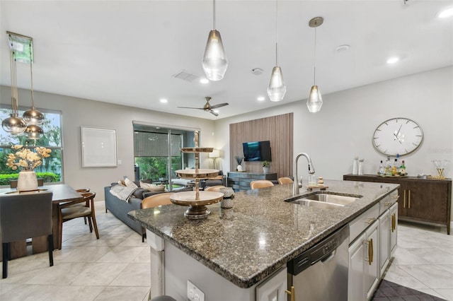 kitchen featuring pendant lighting, an island with sink, sink, dishwasher, and dark stone countertops