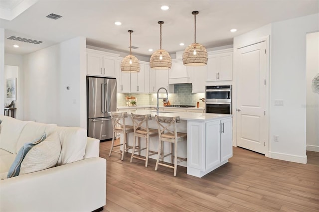 kitchen featuring a kitchen island with sink, white cabinets, decorative light fixtures, a breakfast bar, and stainless steel appliances