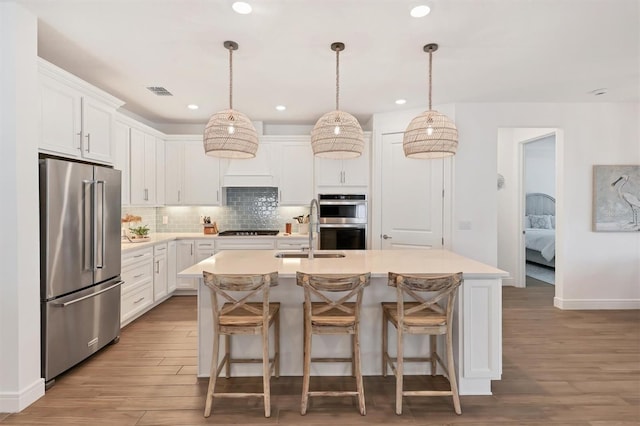 kitchen with pendant lighting, white cabinetry, stainless steel appliances, sink, and a kitchen island with sink