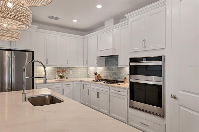 kitchen featuring appliances with stainless steel finishes, decorative light fixtures, white cabinetry, tasteful backsplash, and premium range hood