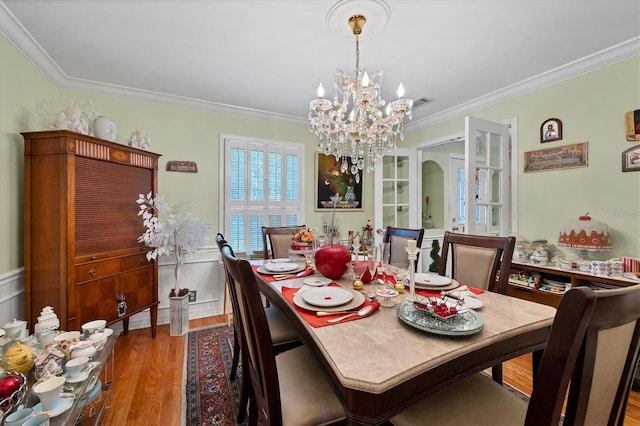 dining room featuring arched walkways, crown molding, wood finished floors, and an inviting chandelier