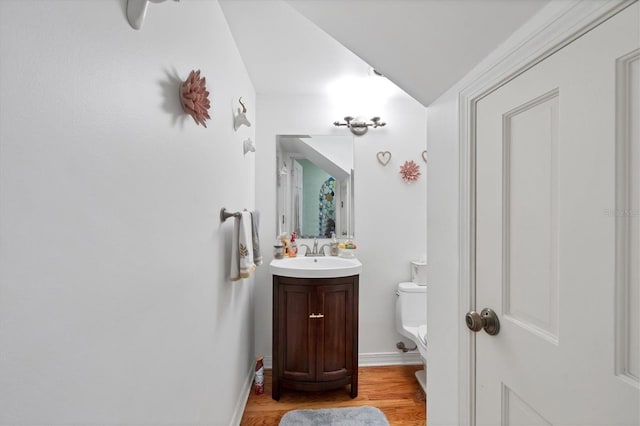 half bath featuring vanity, wood finished floors, toilet, and baseboards