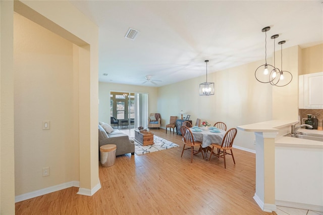 dining space with light wood-type flooring, sink, and ceiling fan with notable chandelier