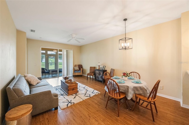 dining area with ceiling fan with notable chandelier and wood-type flooring