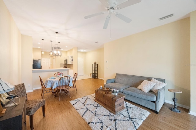 living room with light wood-type flooring and ceiling fan with notable chandelier