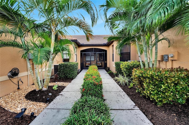entrance to property featuring stucco siding, a tile roof, and central AC