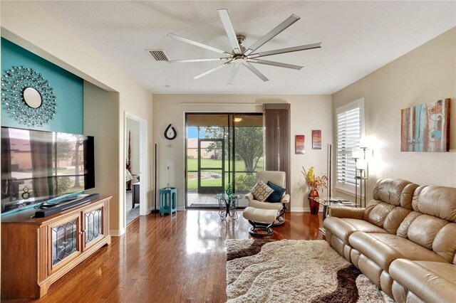 living area featuring a ceiling fan, visible vents, baseboards, and wood finished floors