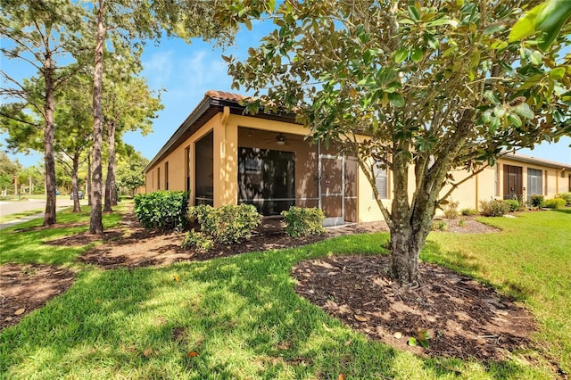 view of front of home featuring stucco siding, a sunroom, a ceiling fan, and a front yard