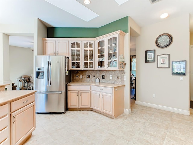 kitchen featuring stainless steel fridge with ice dispenser, backsplash, and a skylight