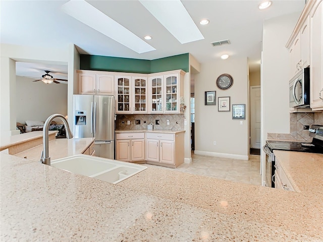 kitchen featuring a skylight, ceiling fan, stainless steel appliances, light stone counters, and decorative backsplash