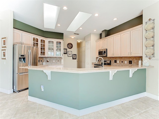 kitchen featuring kitchen peninsula, a kitchen bar, a skylight, and stainless steel appliances