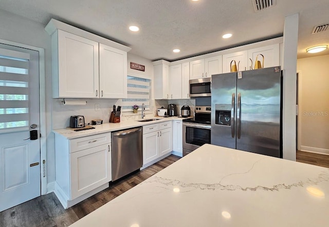 kitchen featuring dark hardwood / wood-style floors, sink, light stone countertops, white cabinets, and appliances with stainless steel finishes