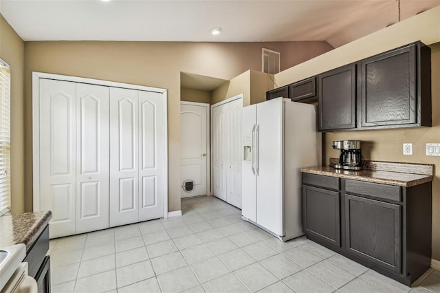 kitchen with dark brown cabinets, lofted ceiling, white fridge with ice dispenser, and light tile patterned floors