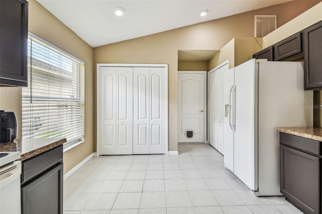 kitchen with dark brown cabinets, vaulted ceiling, white refrigerator with ice dispenser, and light tile patterned floors