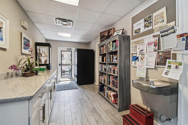 interior space with light hardwood / wood-style floors, a drop ceiling, light stone countertops, and white cabinets