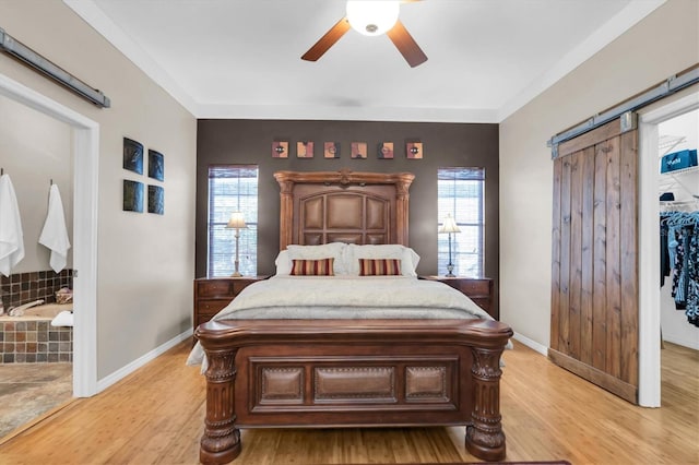 bedroom featuring a barn door, multiple windows, light hardwood / wood-style floors, and ceiling fan