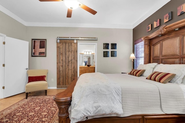 bedroom featuring ceiling fan, ornamental molding, ensuite bathroom, and a barn door