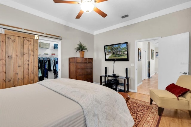 bedroom with a closet, a spacious closet, a barn door, light wood-type flooring, and ceiling fan