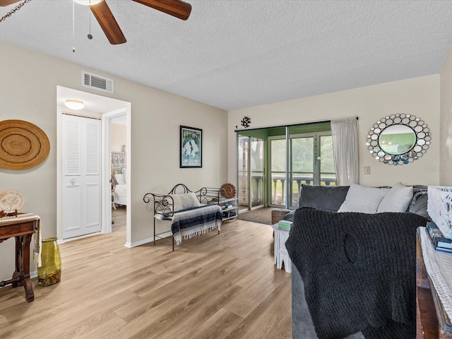 living room with a textured ceiling, light wood-type flooring, and ceiling fan