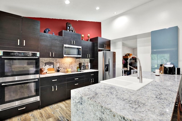 kitchen with light stone countertops, sink, tasteful backsplash, appliances with stainless steel finishes, and light wood-type flooring