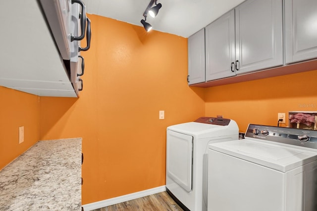 laundry area with cabinets, washing machine and dryer, light hardwood / wood-style floors, and rail lighting