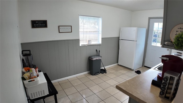 kitchen featuring wooden walls, white refrigerator, and light tile patterned floors