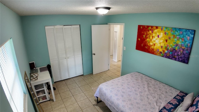 bedroom featuring a textured ceiling, vaulted ceiling, light tile patterned floors, and a closet