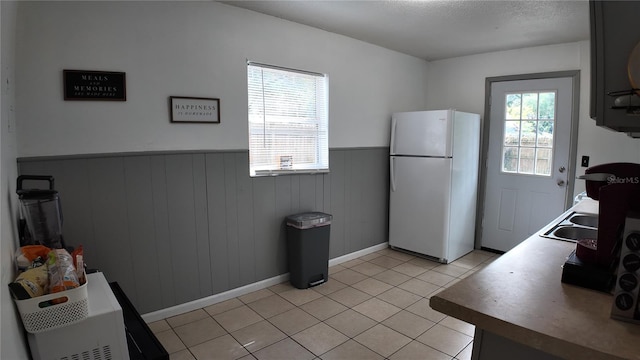 kitchen with light tile patterned flooring, wood walls, white fridge, and a wealth of natural light