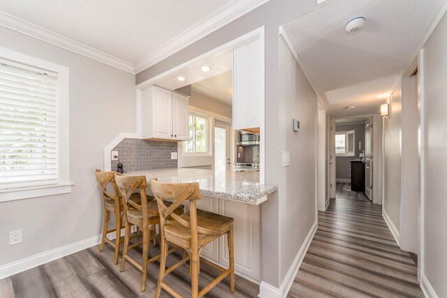 kitchen with kitchen peninsula, backsplash, white cabinetry, a kitchen bar, and dark hardwood / wood-style floors