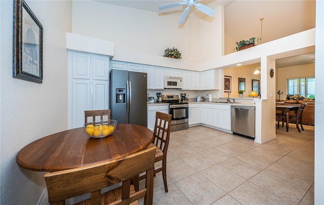 kitchen with stainless steel appliances, light tile patterned floors, high vaulted ceiling, white cabinets, and ceiling fan