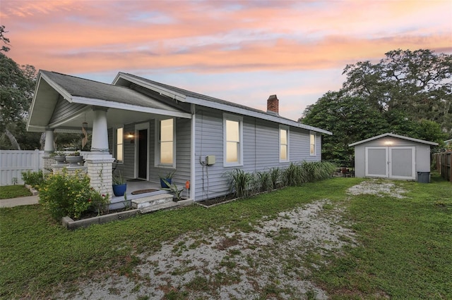 property exterior at dusk featuring a lawn, a storage unit, and covered porch