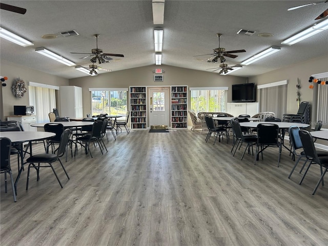 dining room featuring ceiling fan, vaulted ceiling, light hardwood / wood-style floors, and a textured ceiling