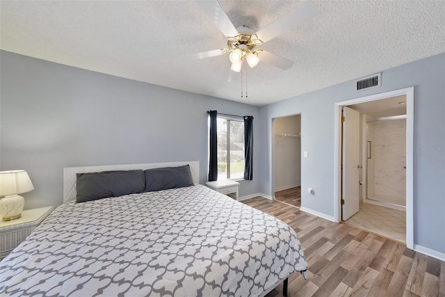 bedroom with a closet, a walk in closet, light wood-type flooring, a textured ceiling, and ceiling fan